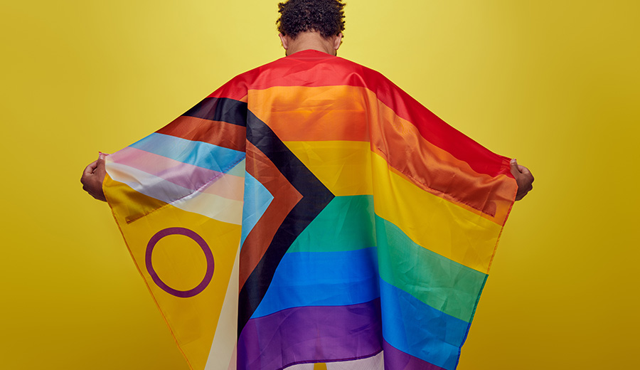 back view of african american person holding rainbow lgbt flag on yellow background.