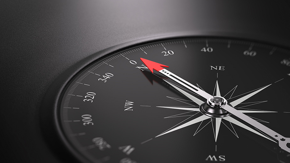 A sleek modern compass sitting on a black surface - the arrow points north