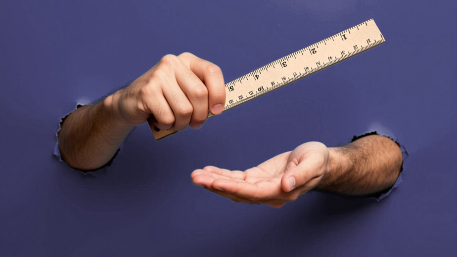 an image of two arms stuck through holes in a paper background, the hands are holding a ruler